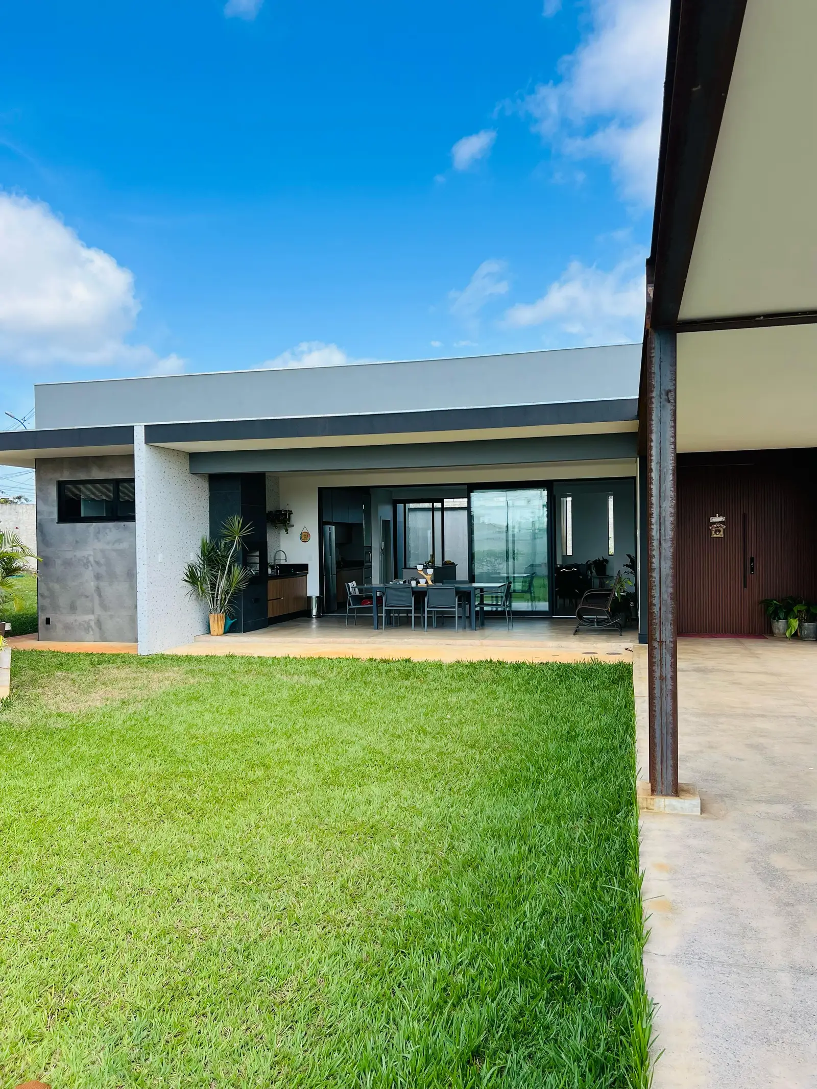 Fachada de fundos da casa térrea do Jardim Botânico: volumes de cobertura plana, grandes vãos de vidro, área gourmet coberta e gramado.