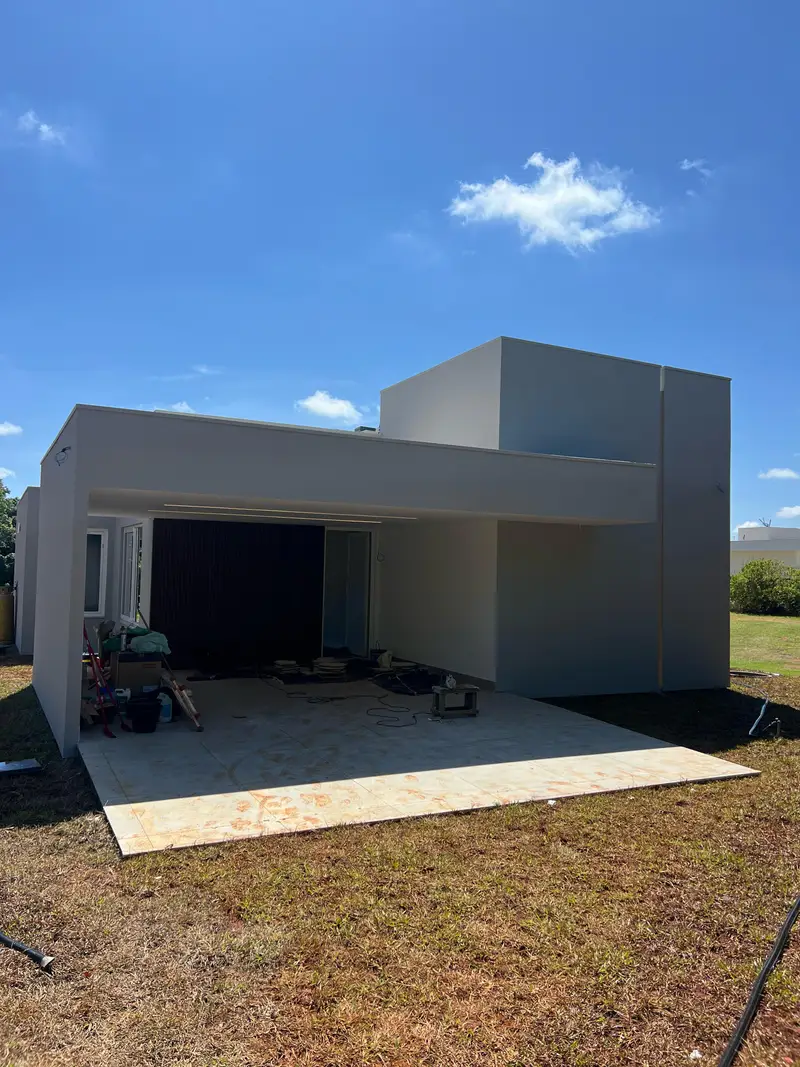 Fachada de fundos da casa do Lago Sul: volumes brancos em concreto aparente e Steel Frame, com terraço coberto e painel ripado preto.