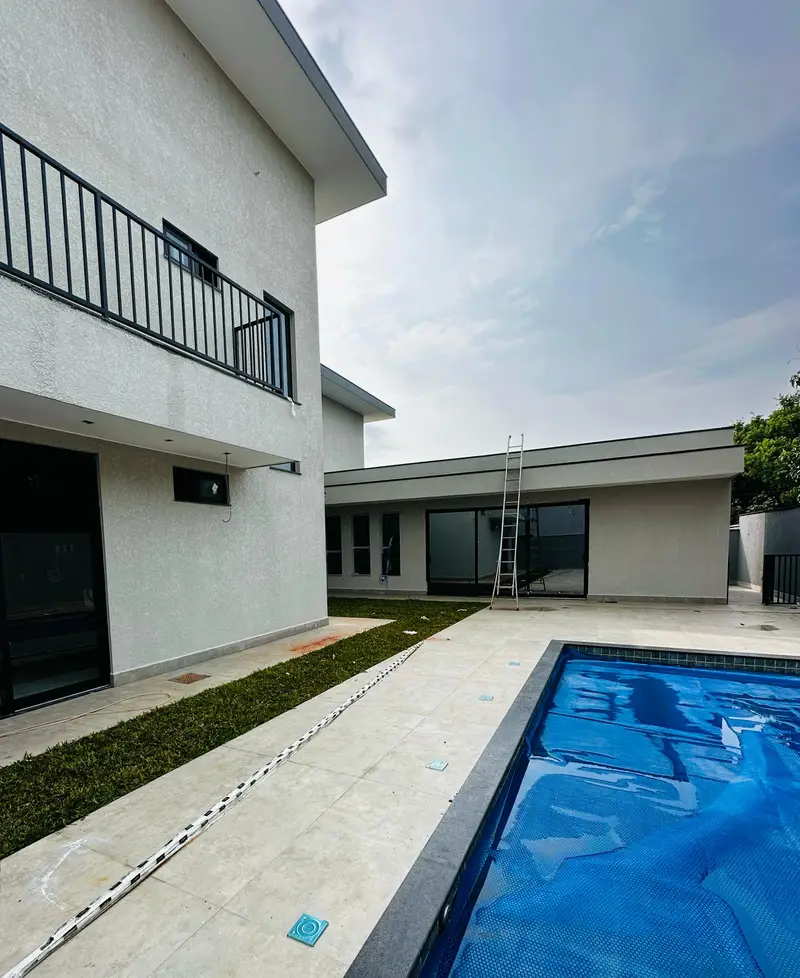 Vista dos fundos da residência com piscina coberta por manta térmica e sacada com guarda-corpo metálico.